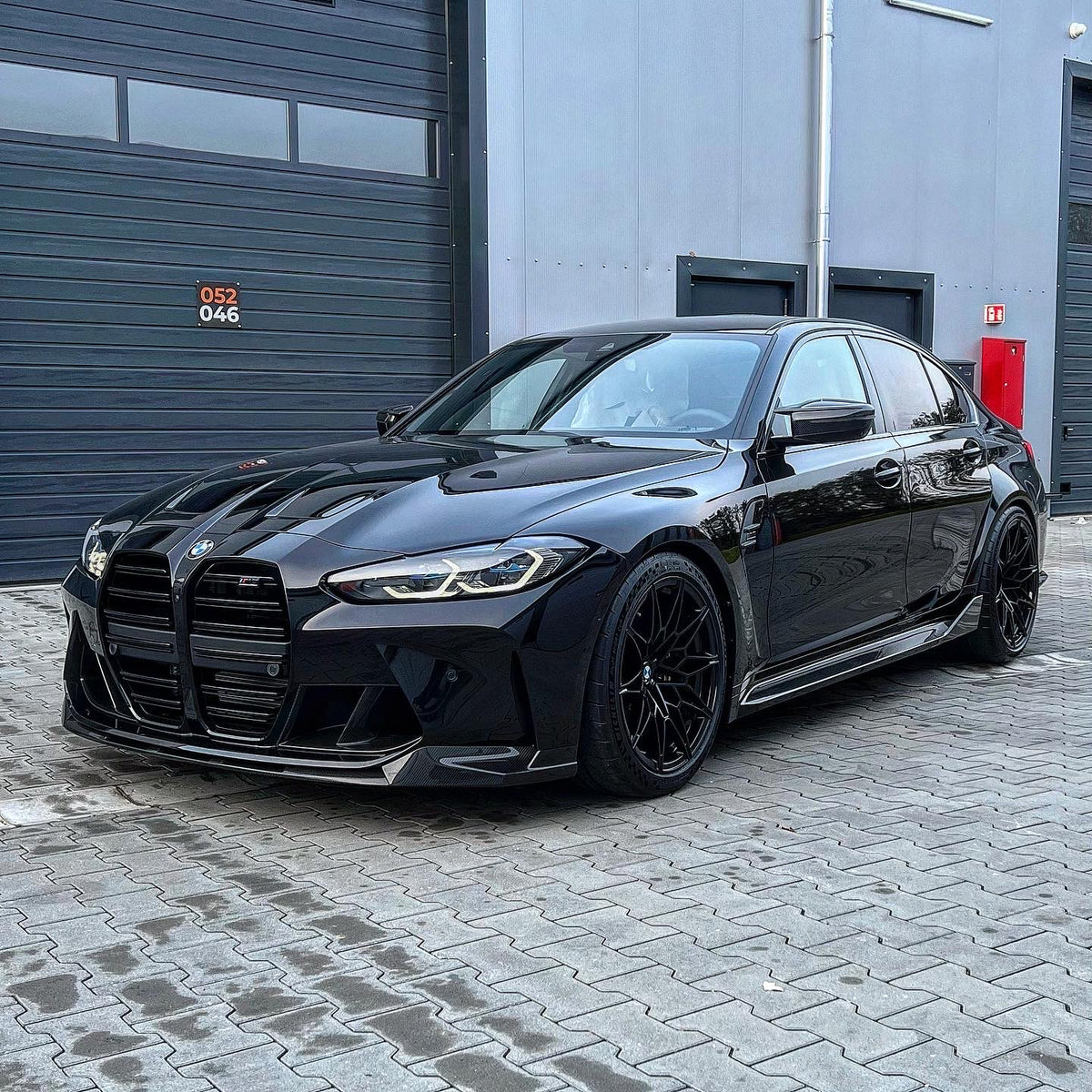 Schwarzer BMW M3 G80 tiefergelegt, Frontansicht schräg vor der Halle